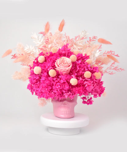 Pink skull with dried flower arrangement including roses, hydrangea, and pampas grass.