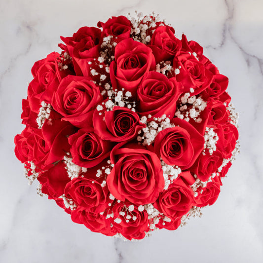 Fresh red roses arranged in a white round hat box with baby’s breath