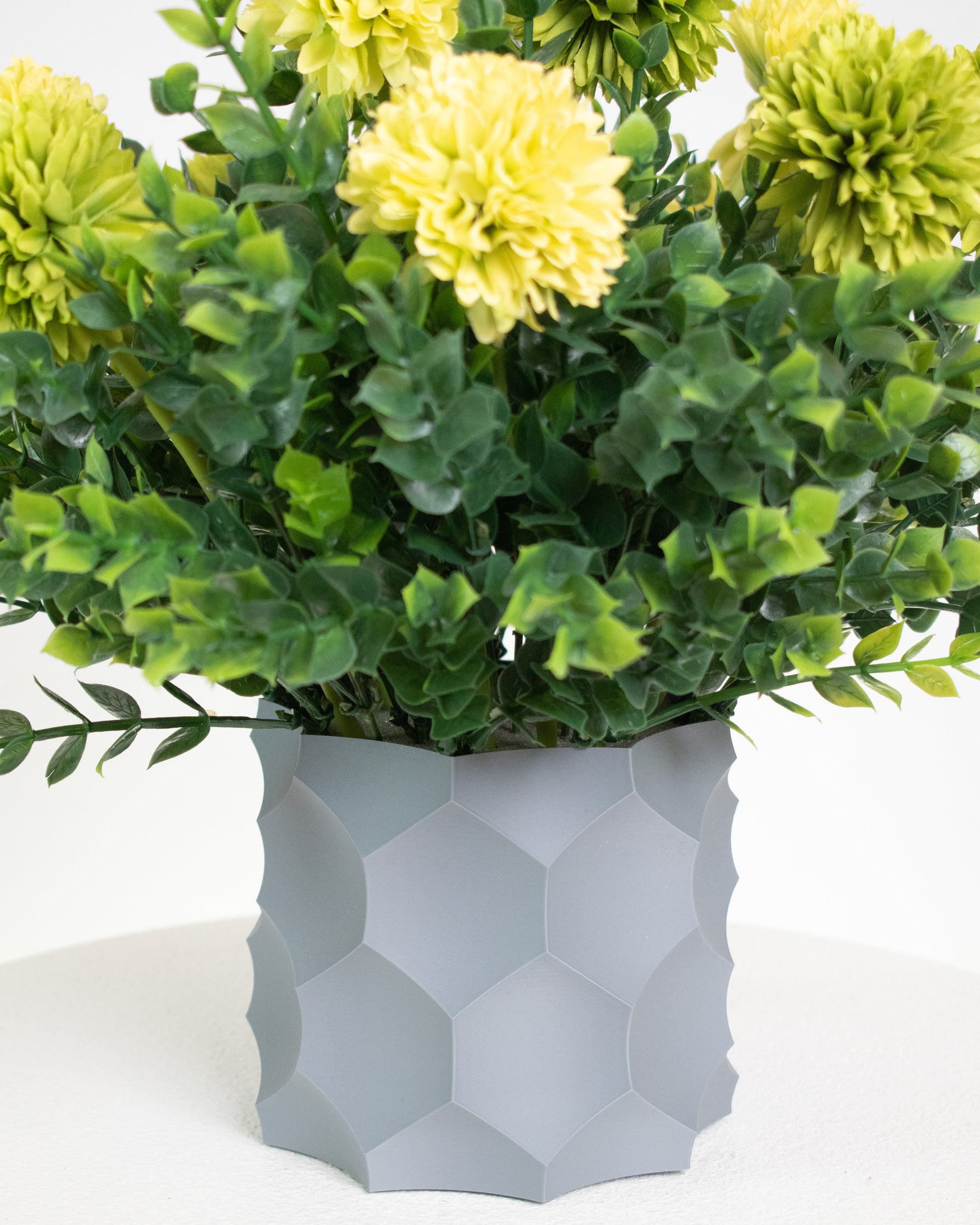 Artificial arrangement with lime-yellow blooms and lush greenery in a modern grey geometric vase