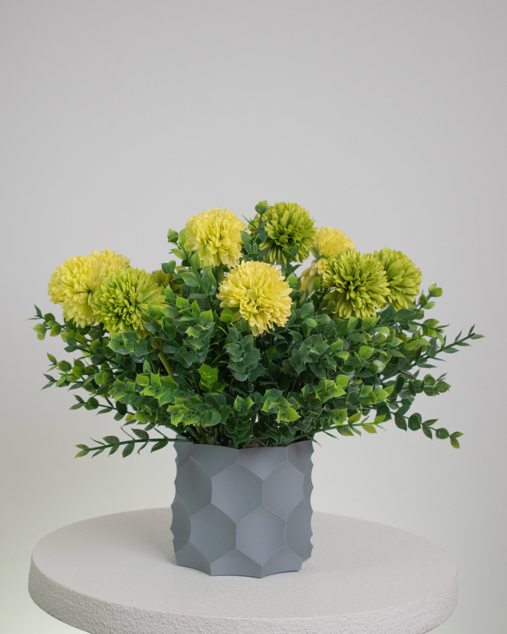 Artificial arrangement with lime-yellow blooms and lush greenery in a modern grey geometric vase