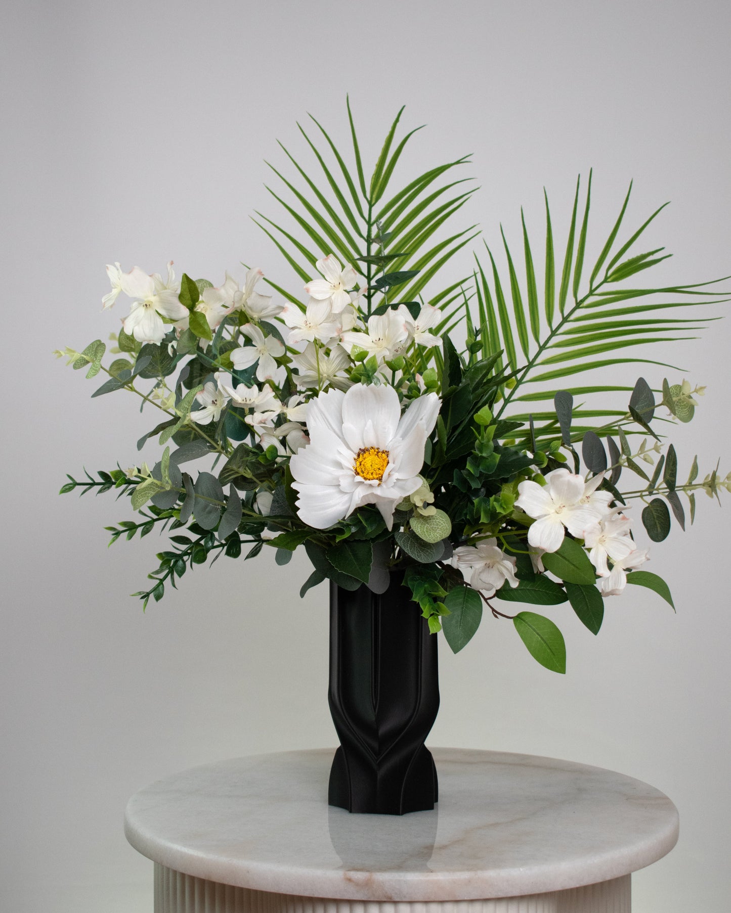Floral arrangement in a black vase on a marble pedestal against a gray background