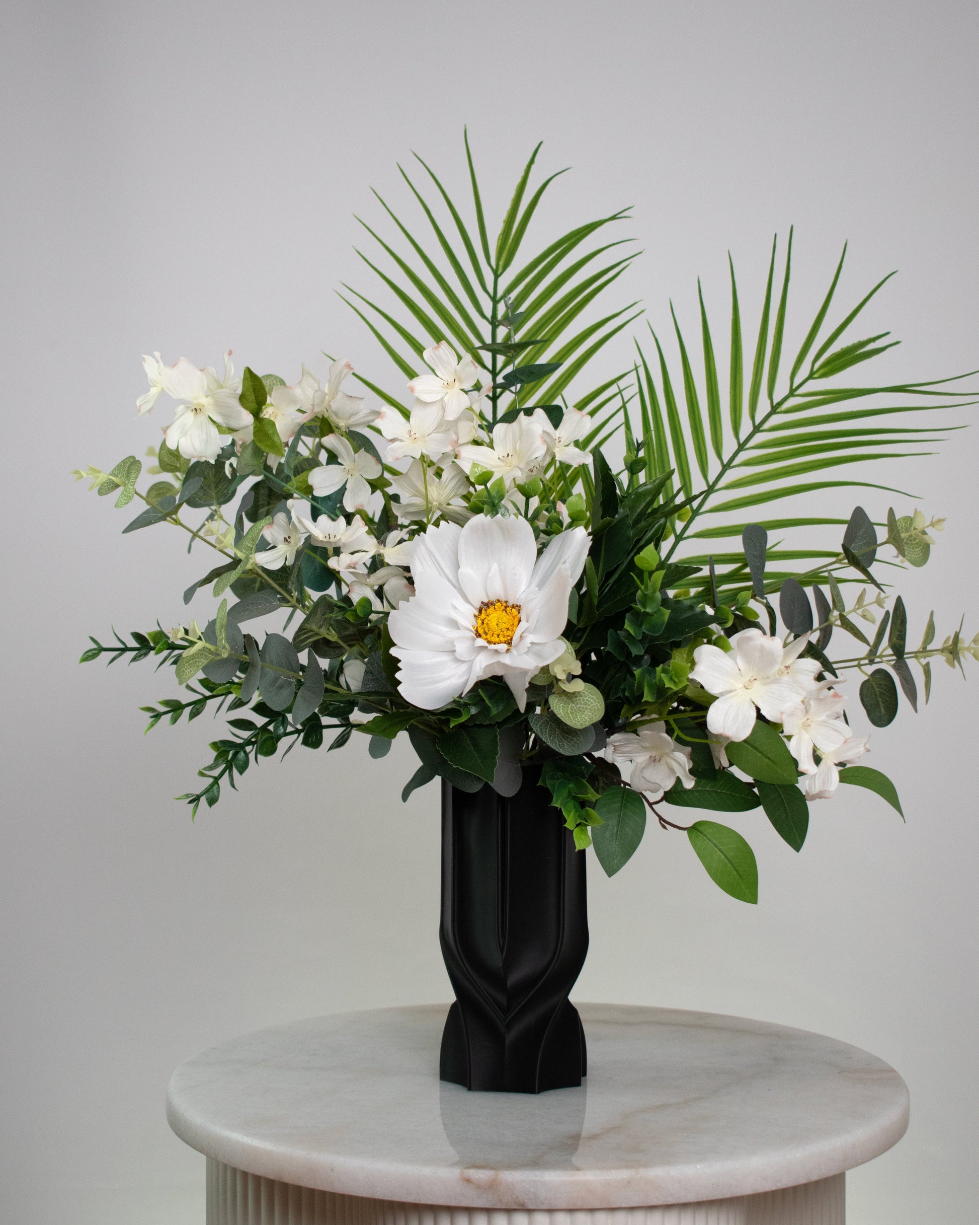 Floral arrangement in a black vase on a marble pedestal against a gray background