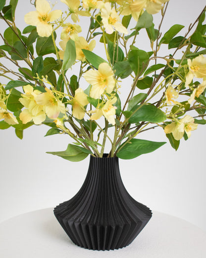Artificial yellow floral arrangement with lush greenery in a modern black pleated vase