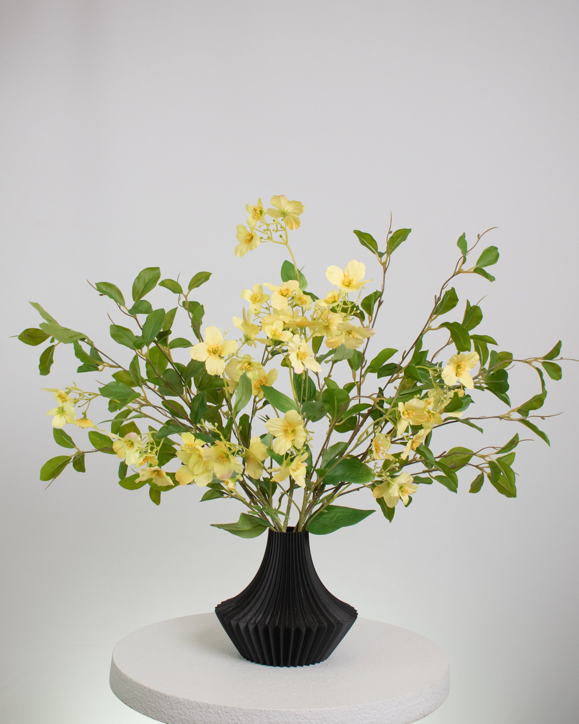 Artificial yellow floral arrangement with lush greenery in a modern black pleated vase