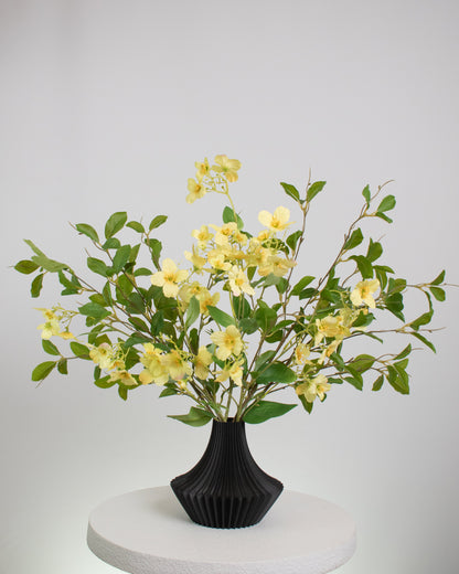 Artificial yellow floral arrangement with lush greenery in a modern black pleated vase