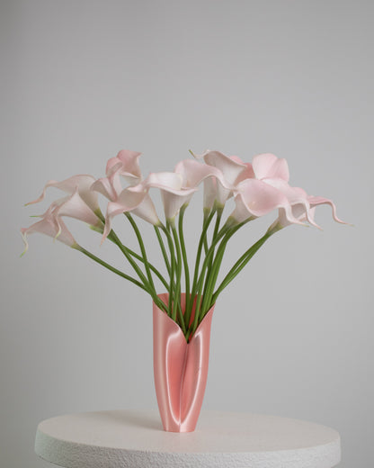 Artificial floral arrangement of soft pink calla lilies with lifelike green stems, elegantly displayed in a sleek blush pink vase on a neutral background
