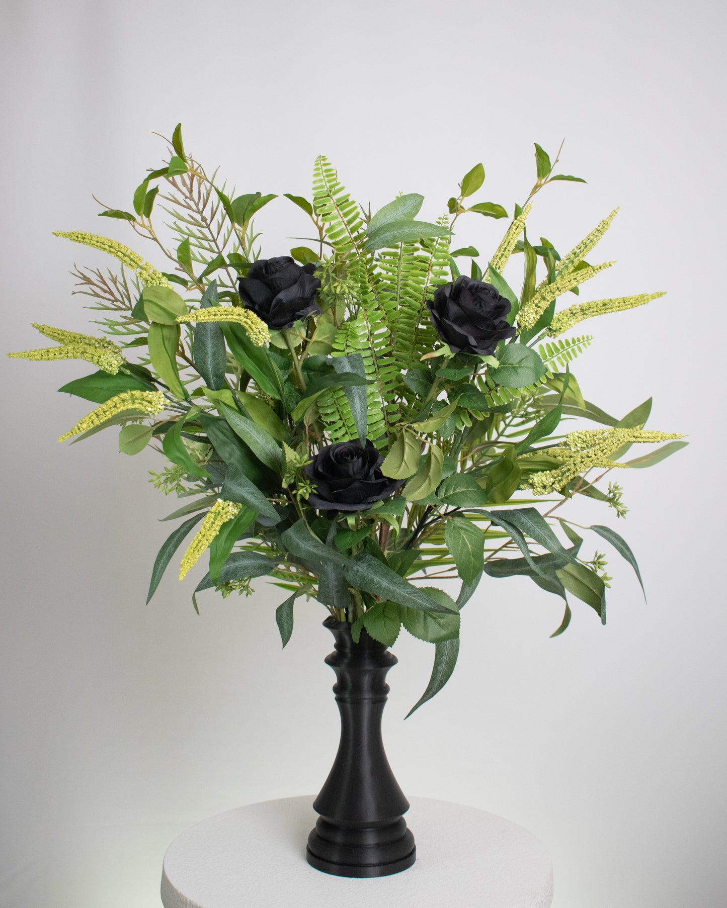 Artificial arrangement with black roses and lush green foliage displayed in a chess-queen–shaped matte-black vase, symbolizing power, sophistication, and modern elegance.
