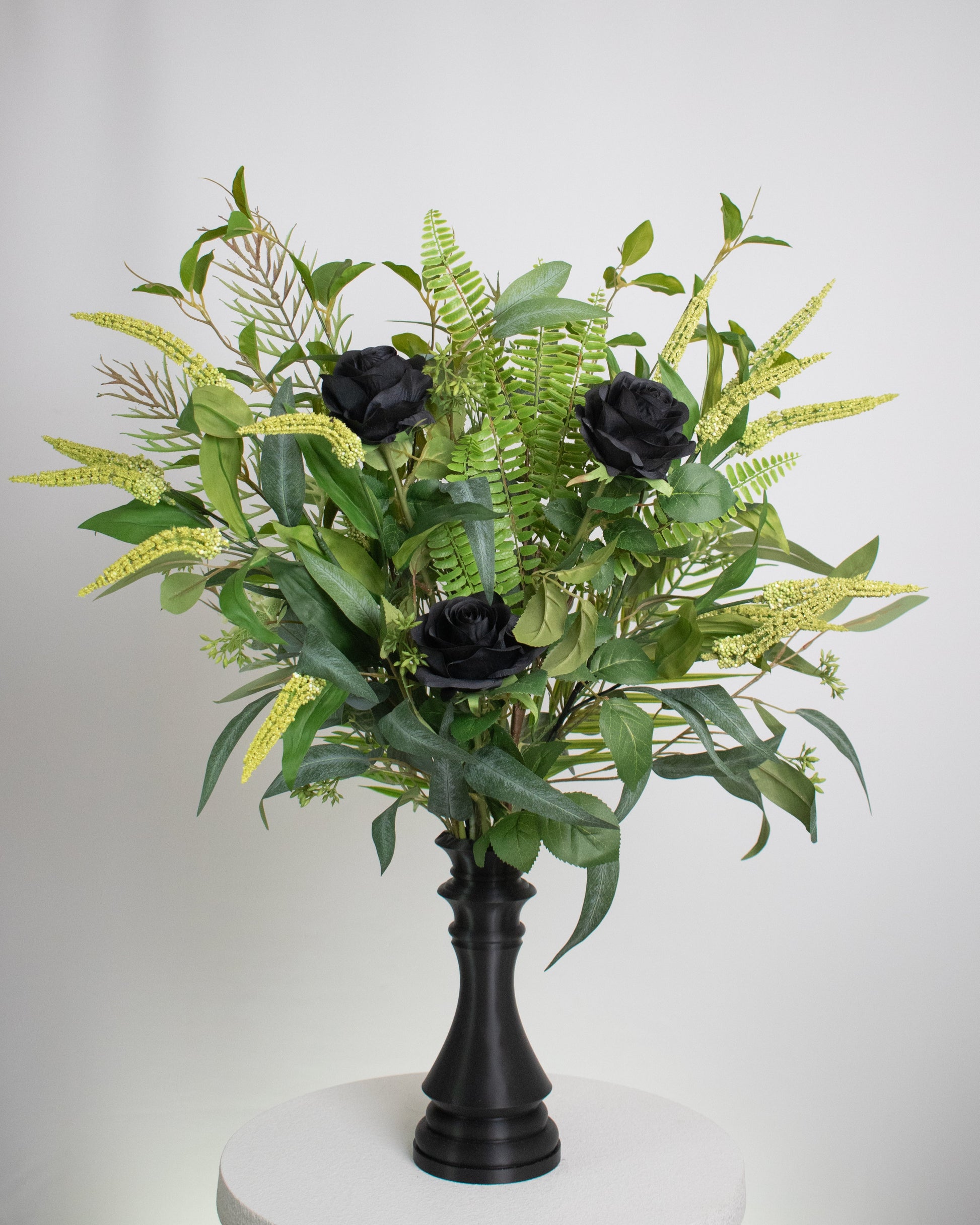 Artificial arrangement with black roses and lush green foliage displayed in a chess-queen–shaped matte-black vase, symbolizing power, sophistication, and modern elegance.