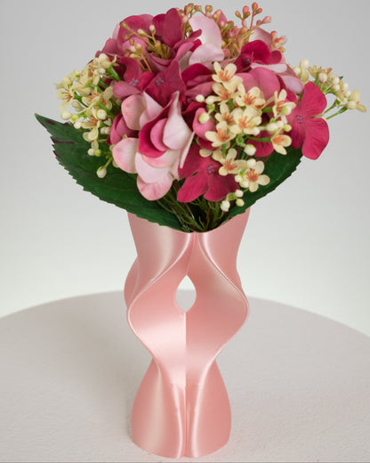 Artificial pink floral arrangement featuring rosy hydrangeas and cream blossoms, beautifully displayed in a sculptural modern pink vase with curved design.