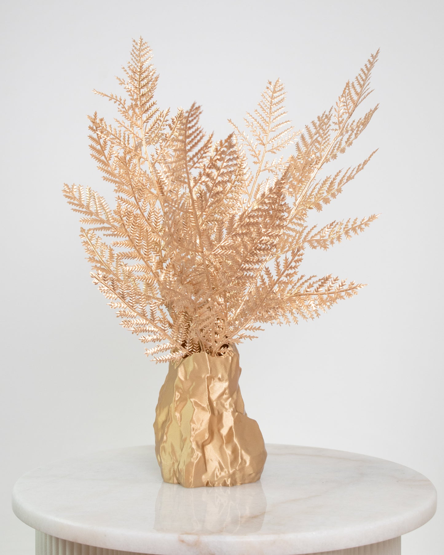 Artificial gold fern arrangement in a sculptural gold vase, styled on a marble table — a modern, luxurious decorative piece ideal for elegant and minimalist interiors.