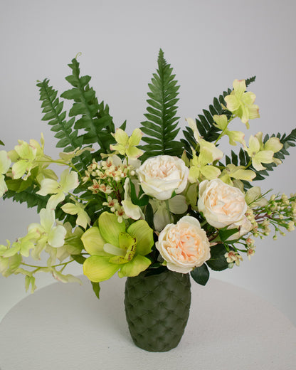 Artificial floral arrangement featuring cream roses, green orchids, and lush ferns in a textured olive-green vase, styled on a white pedestal — perfect for adding a refreshing, natural touch to modern or earthy-toned interiors.