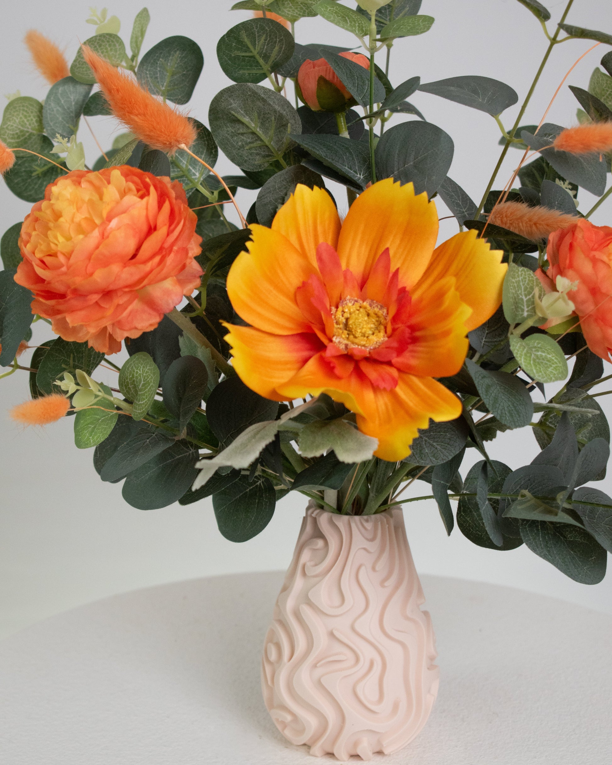 Floral arrangment with the warm orange tones and lush greenery, giving a calm yet lively feeling, perfect for brightening modern or neutral spaces.
