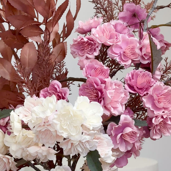 Artificial floral arrangement featuring pink and ivory blossoms with rust-colored foliage, elegantly styled in a tall ribbed nude vase.