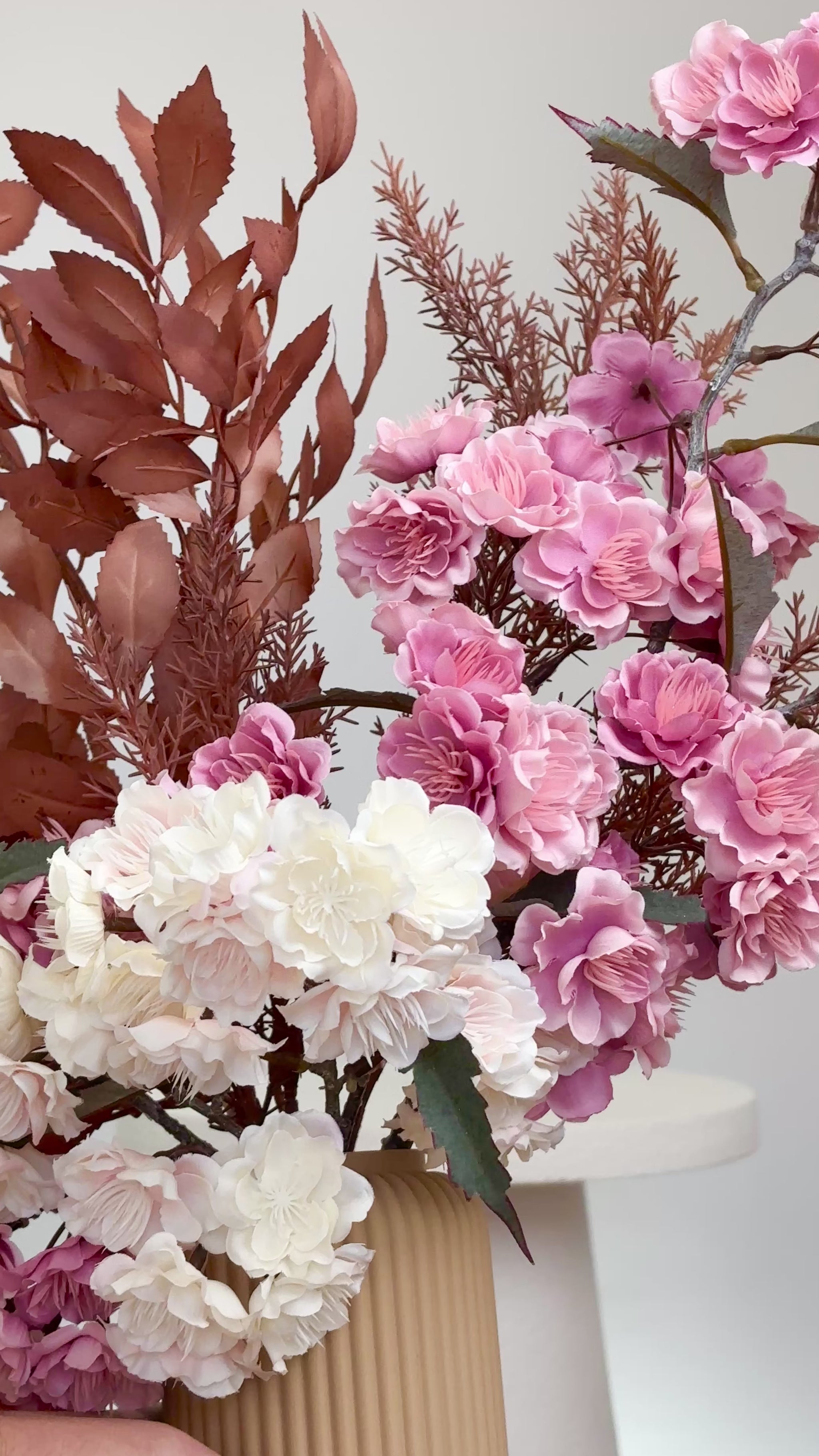 Artificial floral arrangement featuring pink and ivory blossoms with rust-colored foliage, elegantly styled in a tall ribbed nude vase.