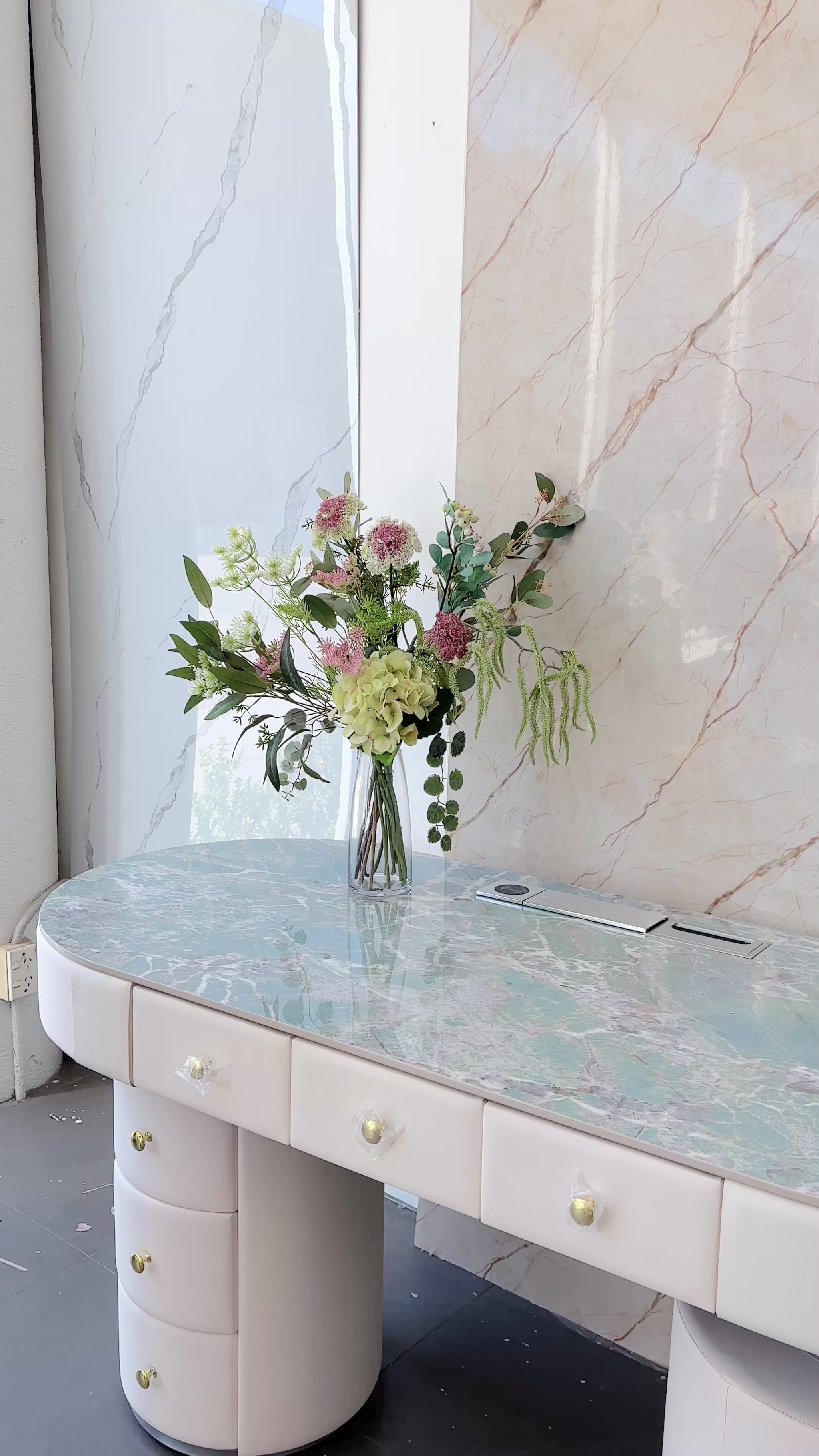 Artificial floral arrangement featuring green hydrangeas, pink wildflowers, and lush foliage in a clear glass vase with acrylic water