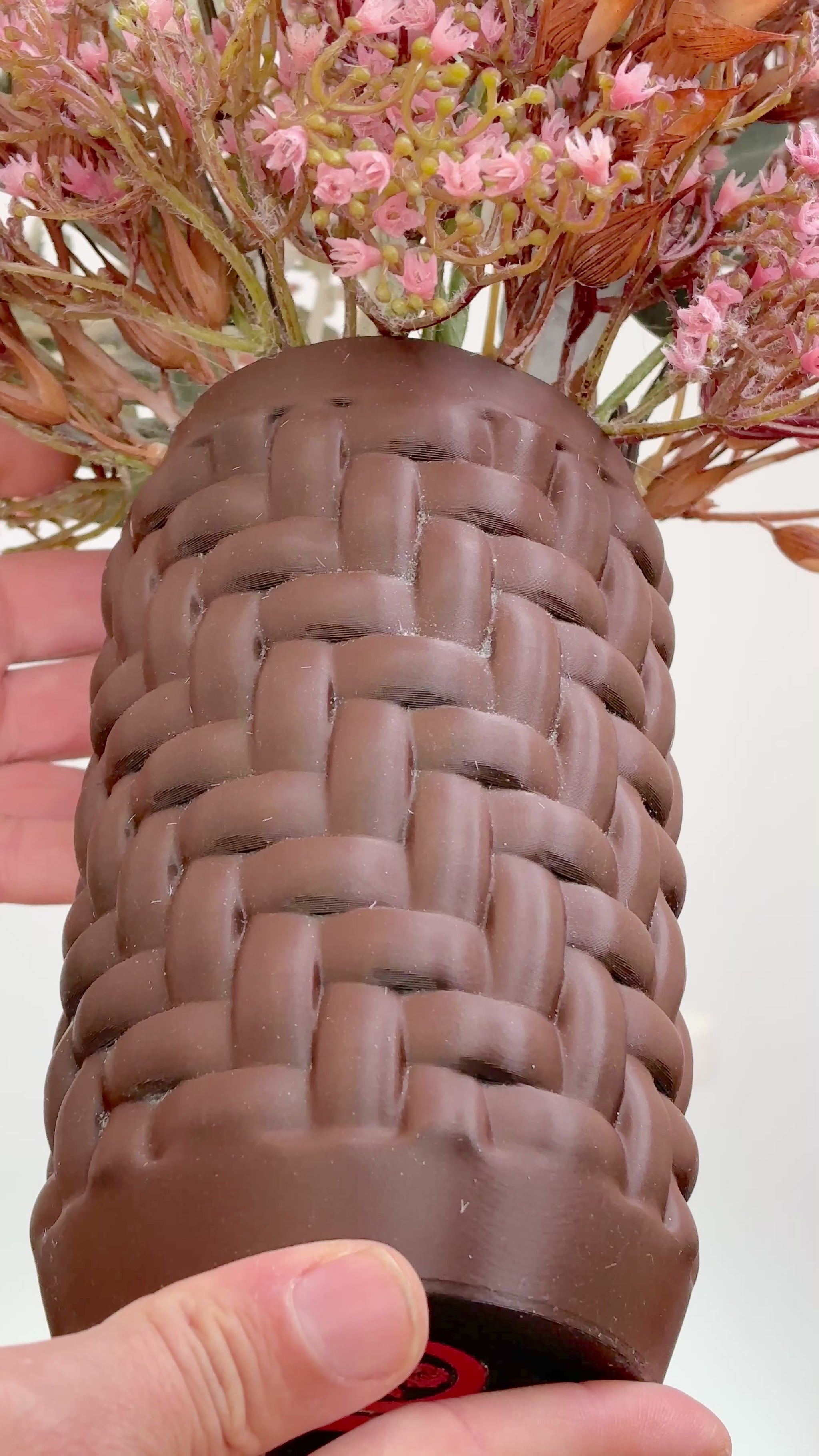 Artificial floral arrangement with blush pink flowers and rustic brown foliage in a woven brown vase, styled on a marble table — a warm, elegant decorative piece perfect for neutral or earthy interiors.