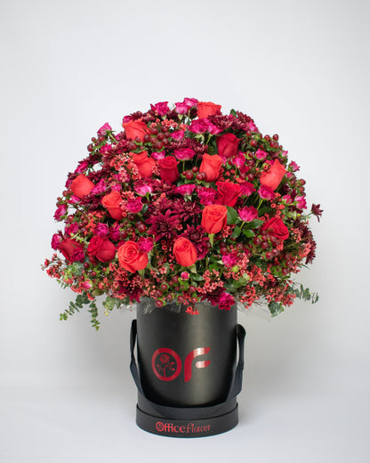 Red rose arrangement in a black gift box with red fillers and black ribbon handles