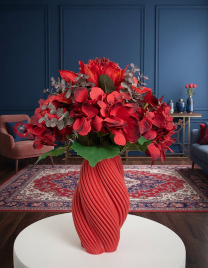 Artificial floral arrangement featuring rich red hydrangeas and crimson blooms with textured foliage, beautifully displayed in a sculptural twisted red vase.