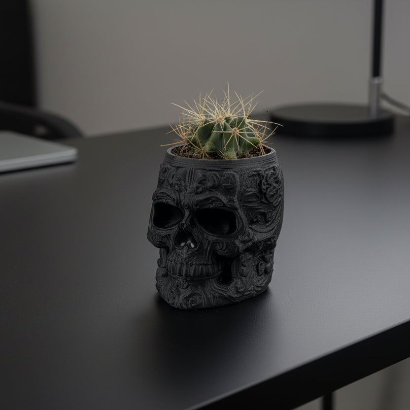 Black skull-shaped planter with a cactus on a gray background.