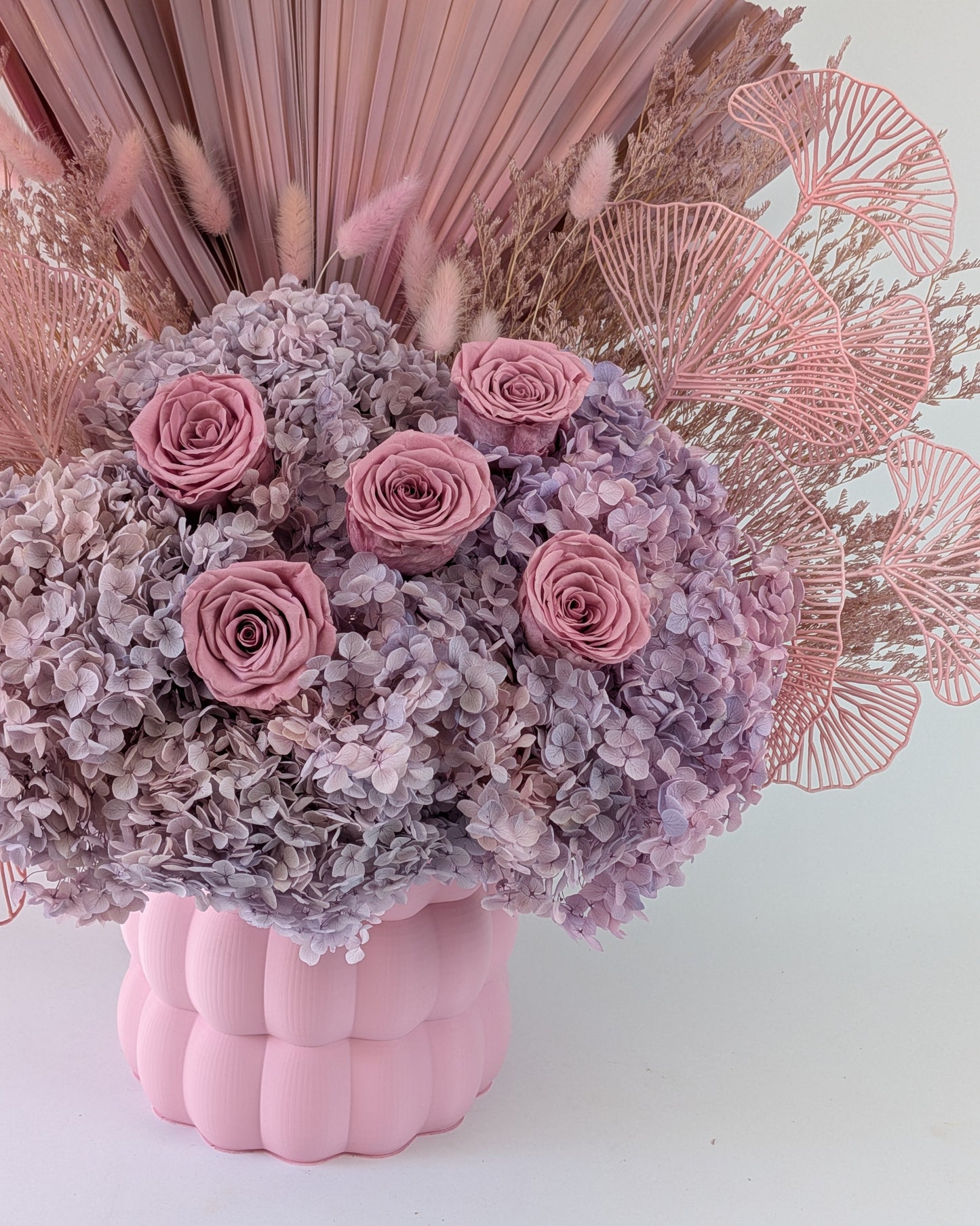 Pink and purple floral arrangement in a pink textured vase against a light background.
