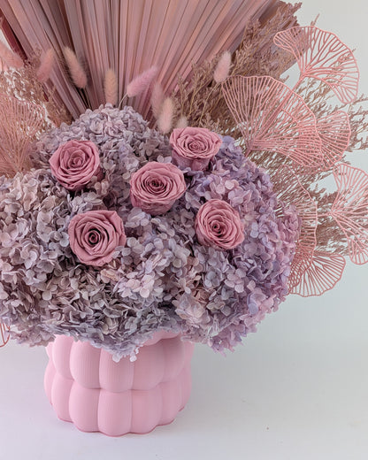 Pink and purple floral arrangement in a pink textured vase against a light background.