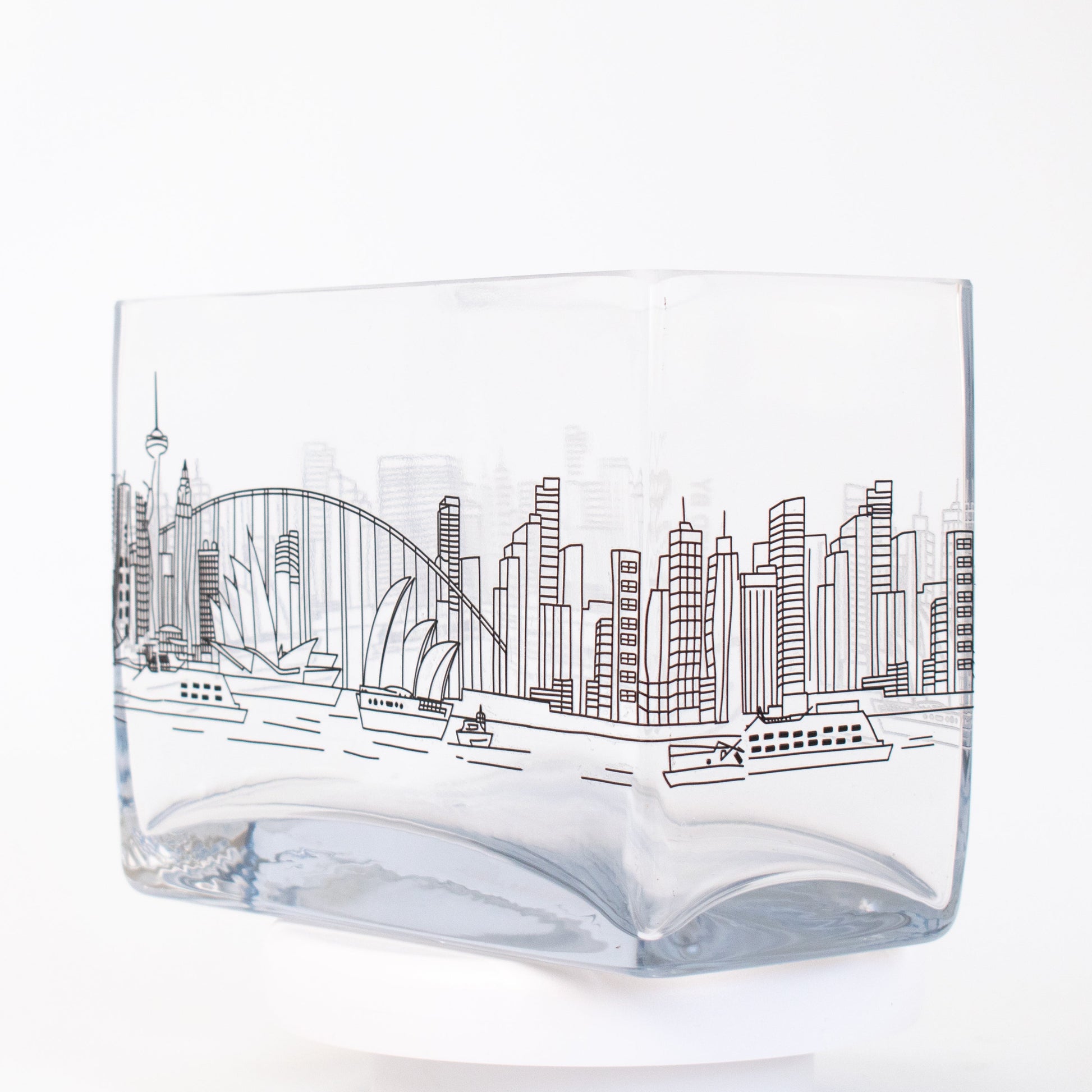 A clear rectangular glass vase featuring a fine-line illustration of the Sydney skyline, including the Opera House, Harbour Bridge, and city buildings.