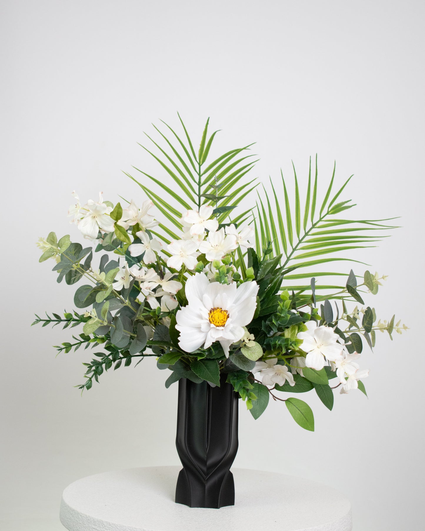 Floral arrangement with white flowers and green leaves in a black vase