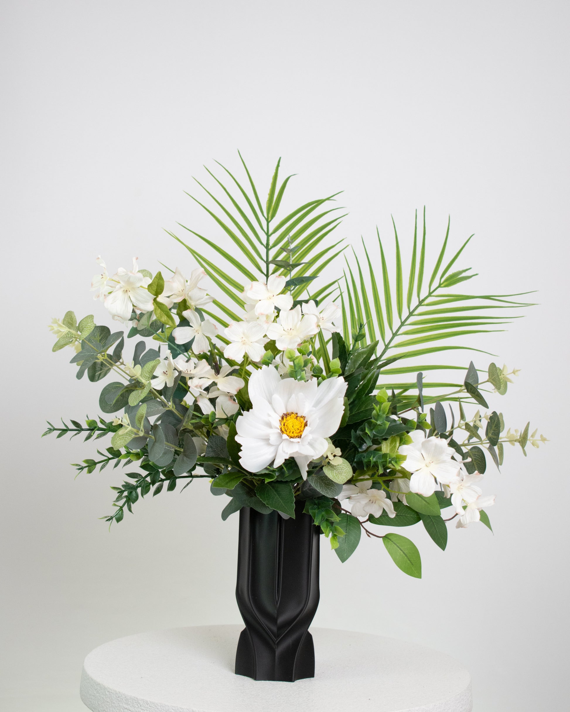 Floral arrangement with white flowers and green leaves in a black vase