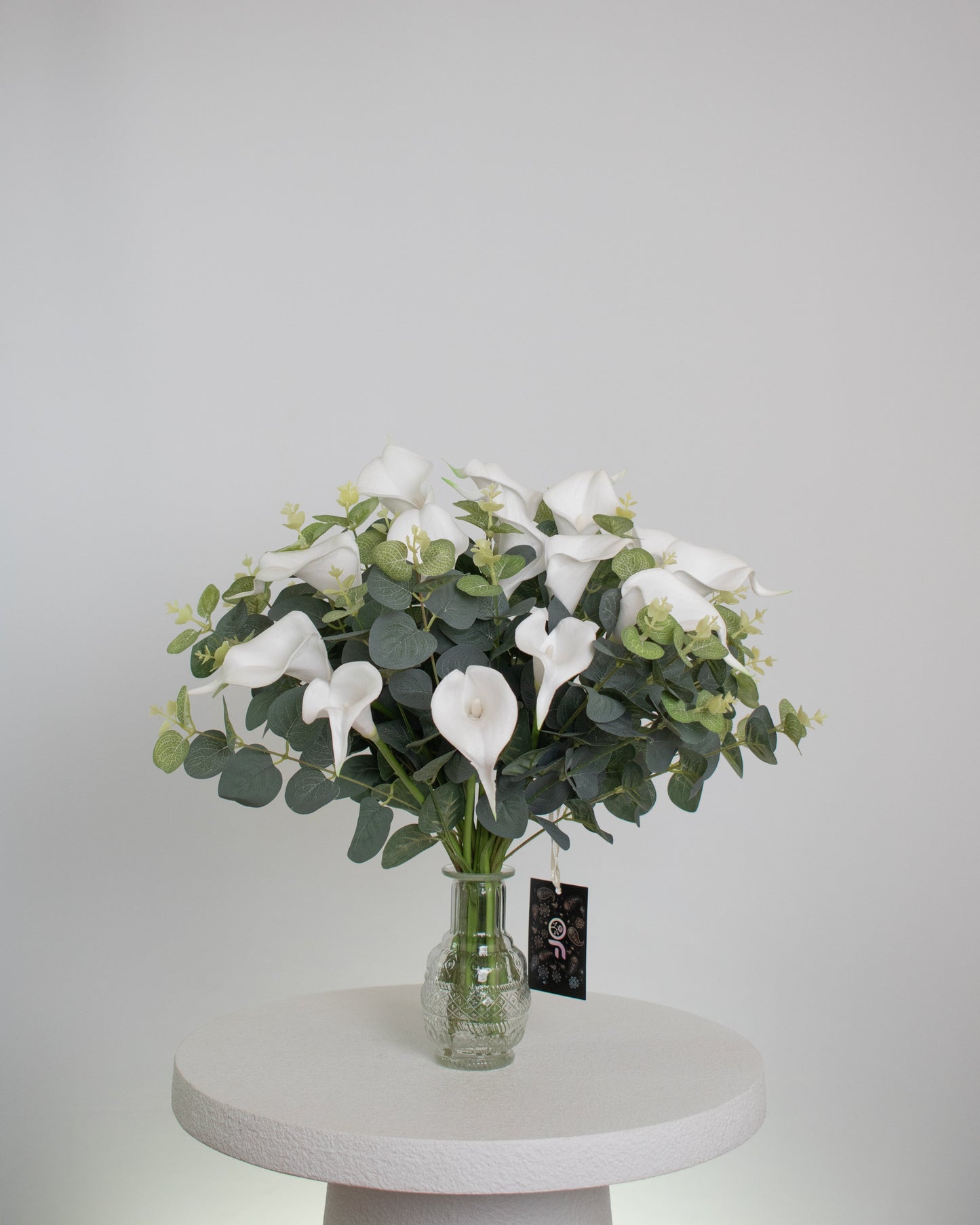 Artificial white calla lily arrangement with lush greenery in a clear glass vase