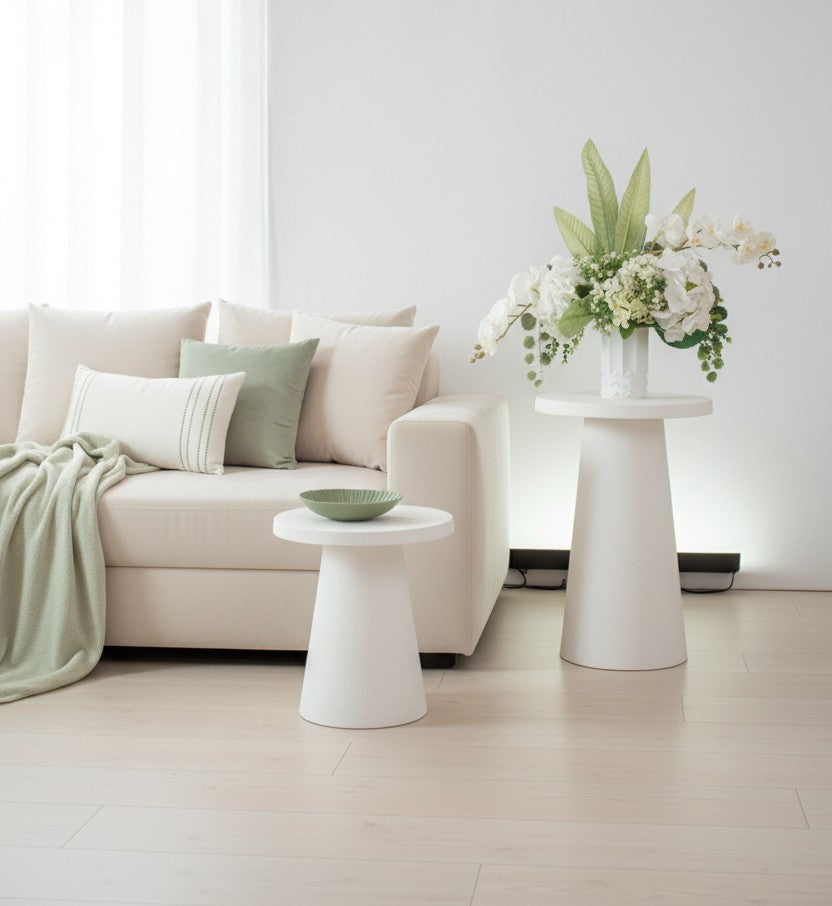 Modern living room with a beige sofa, white tables, and a vase of artificial flowers.